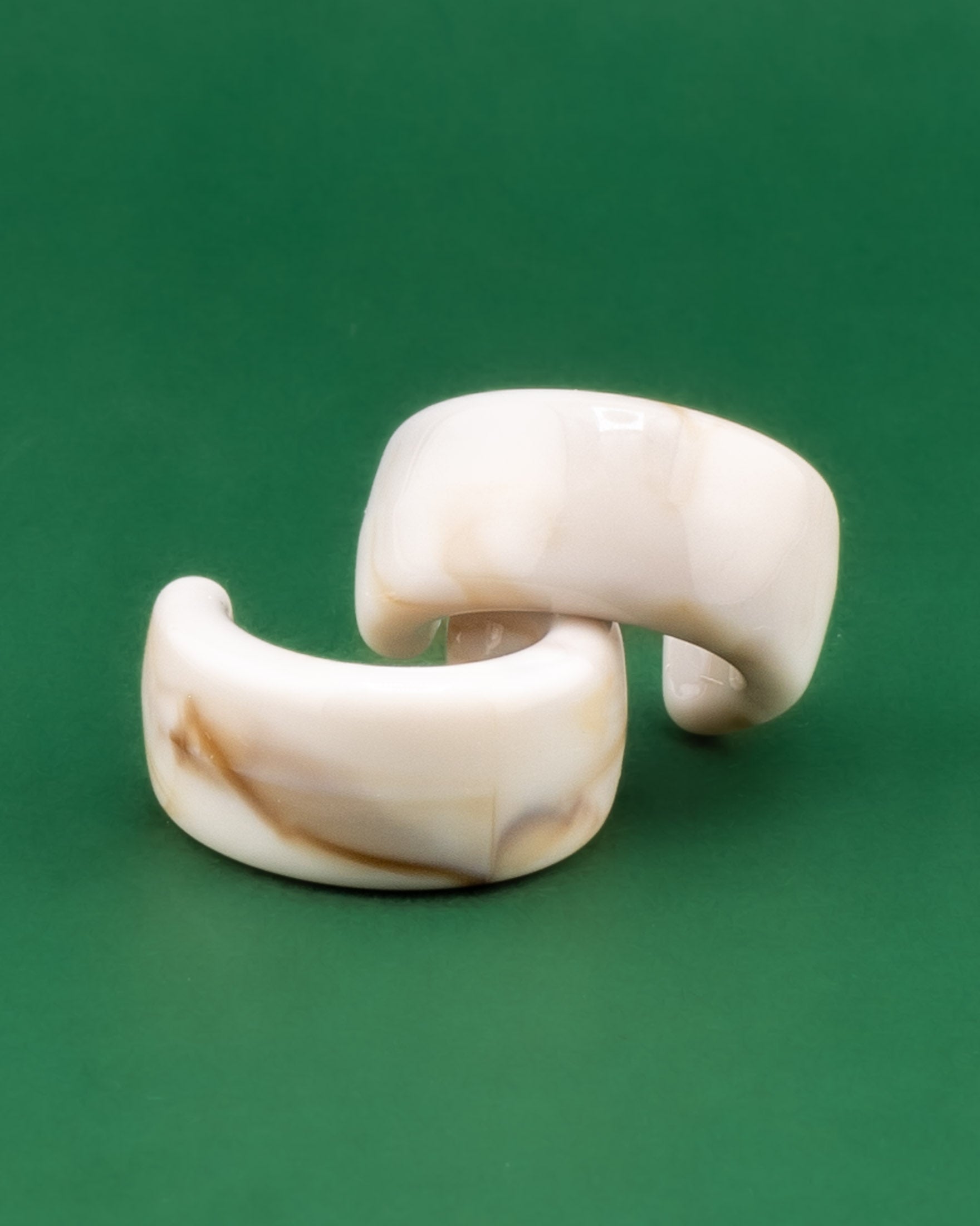 Pair of acrylic cream tortoiseshell earrings on a green background