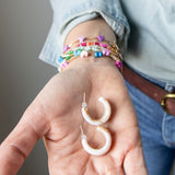 Hand holding a pair of cream tortoiseshell acrylic earrings with colorful bracelets on wrist.