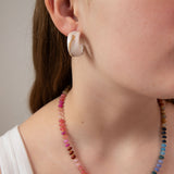 Close-up of a woman wearing a cream tortoiseshell acrylic earring with a colorful beaded necklace.  