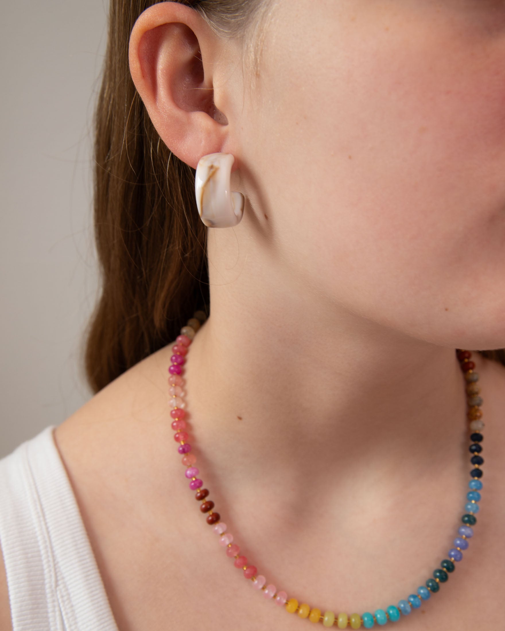Close-up of a woman wearing a cream tortoiseshell acrylic earring with a colorful beaded necklace.  