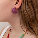 Close-up of a person wearing a purple acrylic hoop earring and colorful beaded necklace.