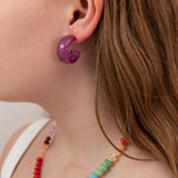 Close-up of a person wearing a purple acrylic hoop earring and colorful beaded necklace.