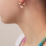 Close-up of a person wearing a pink, white and red striped huggie earring in a heart shape.