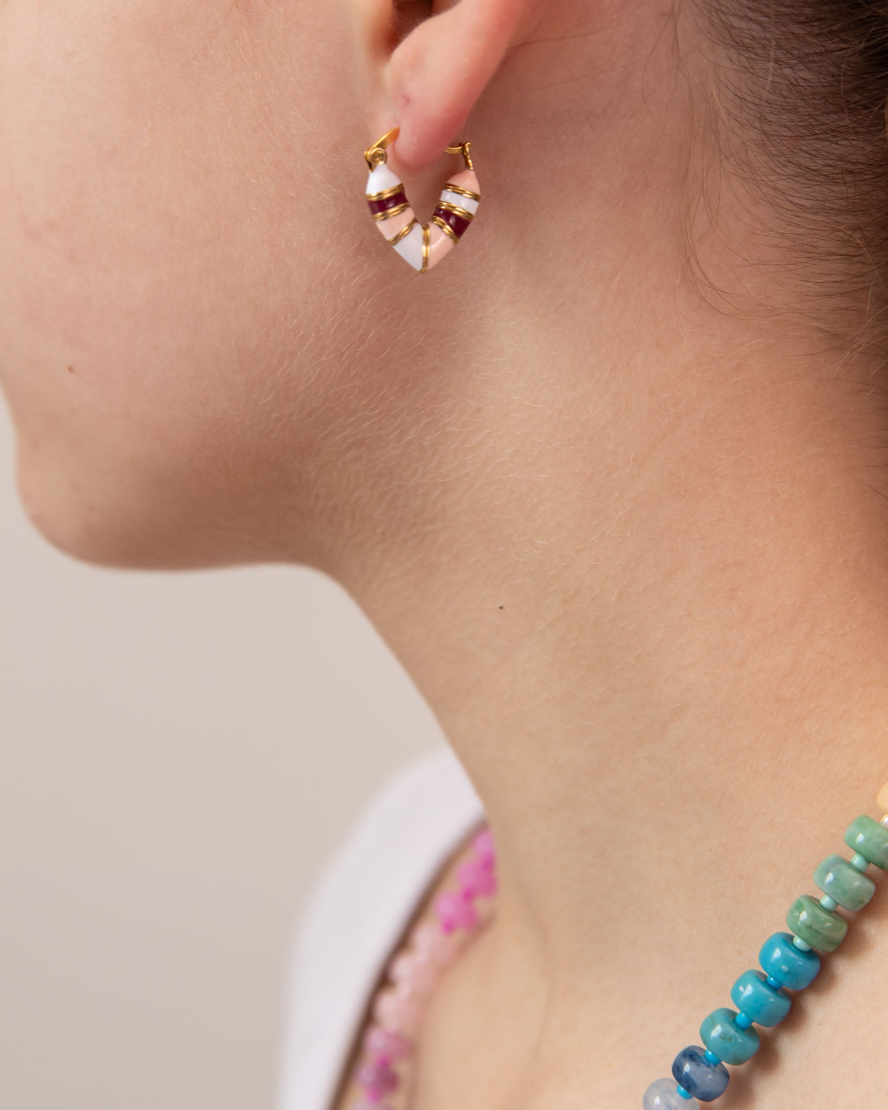 Close-up of a person wearing a pink, white and red striped huggie earring in a heart shape.