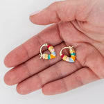 Hand holding two multi-stripe colorful huggie hoop earrings in pink, yellow, orange, blue and green shades