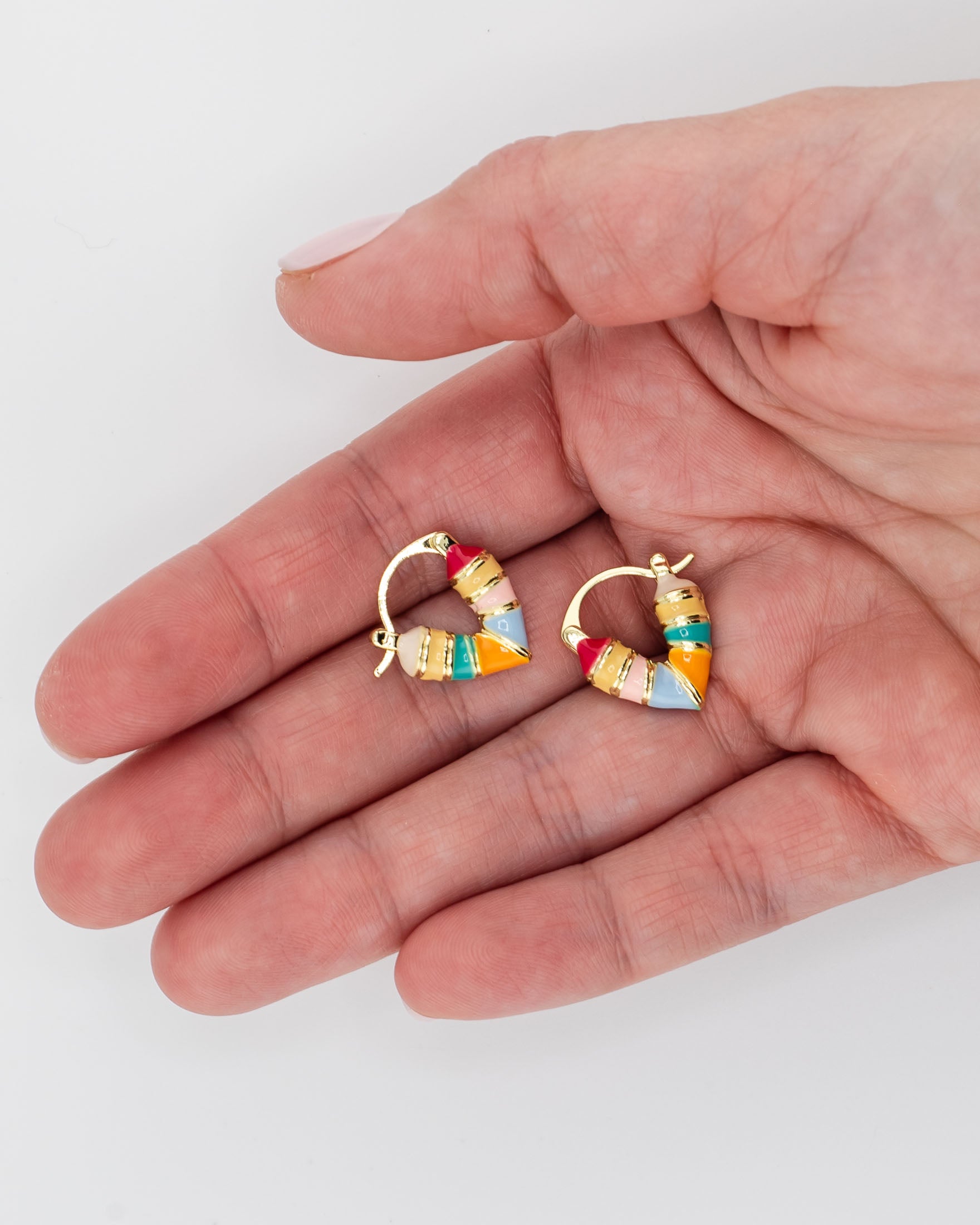 Hand holding two multi-stripe colorful huggie hoop earrings in pink, yellow, orange, blue and green shades