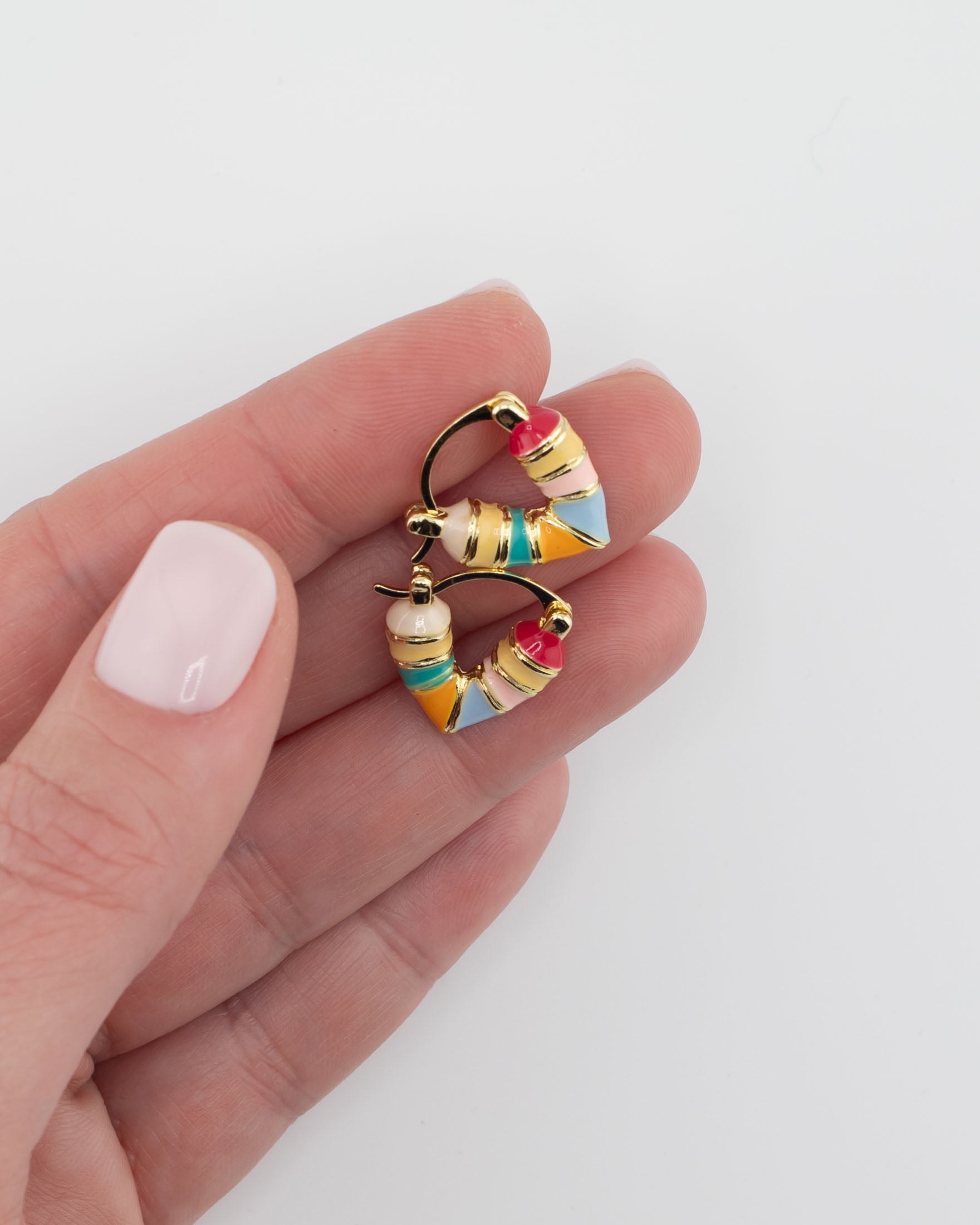 Close up of gold and colorful striped huggie earrings held between fingers by Kaleidoscope Living
