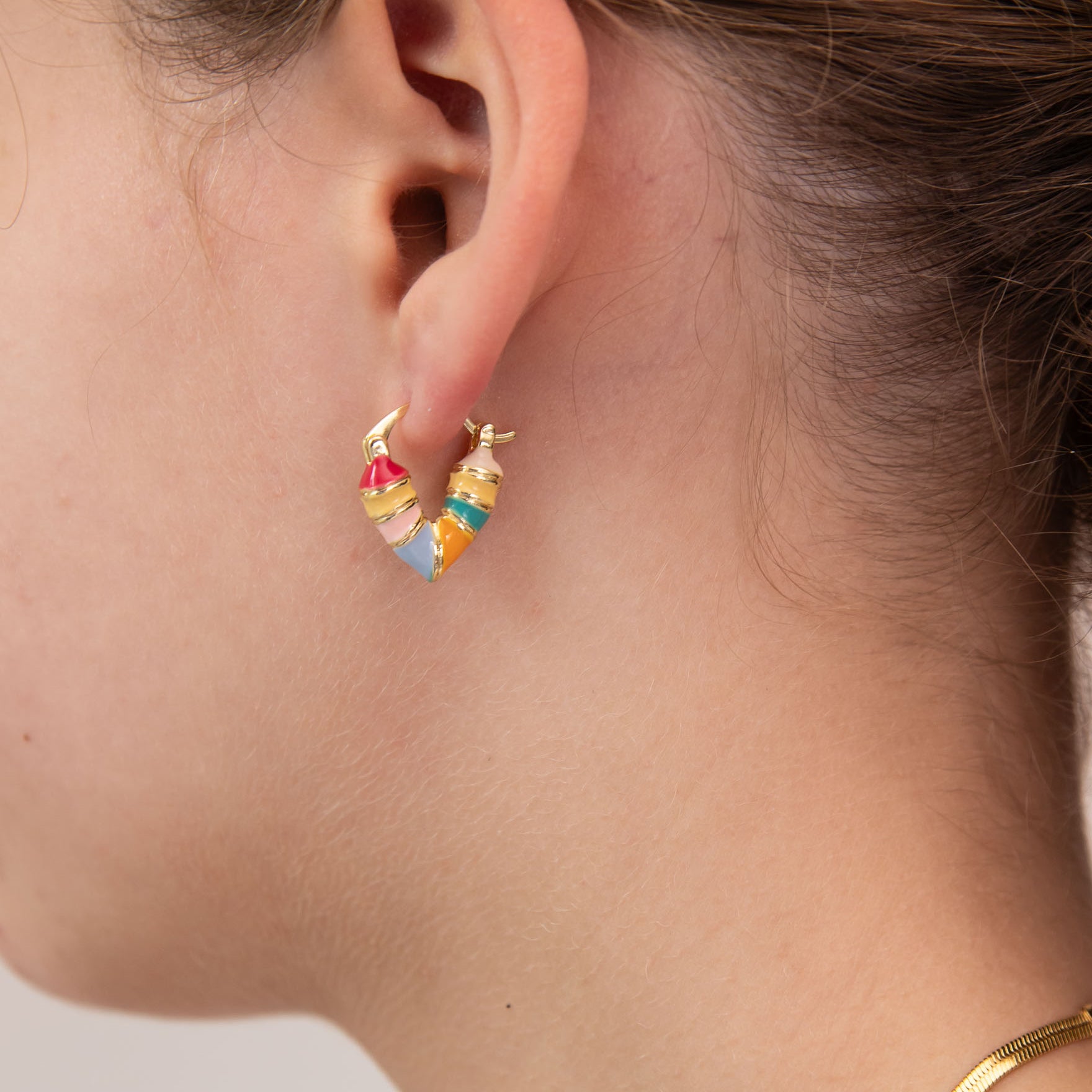 Close-up of a girl wearing colorful heart-shaped huggie earring by Kaleidoscope Living.