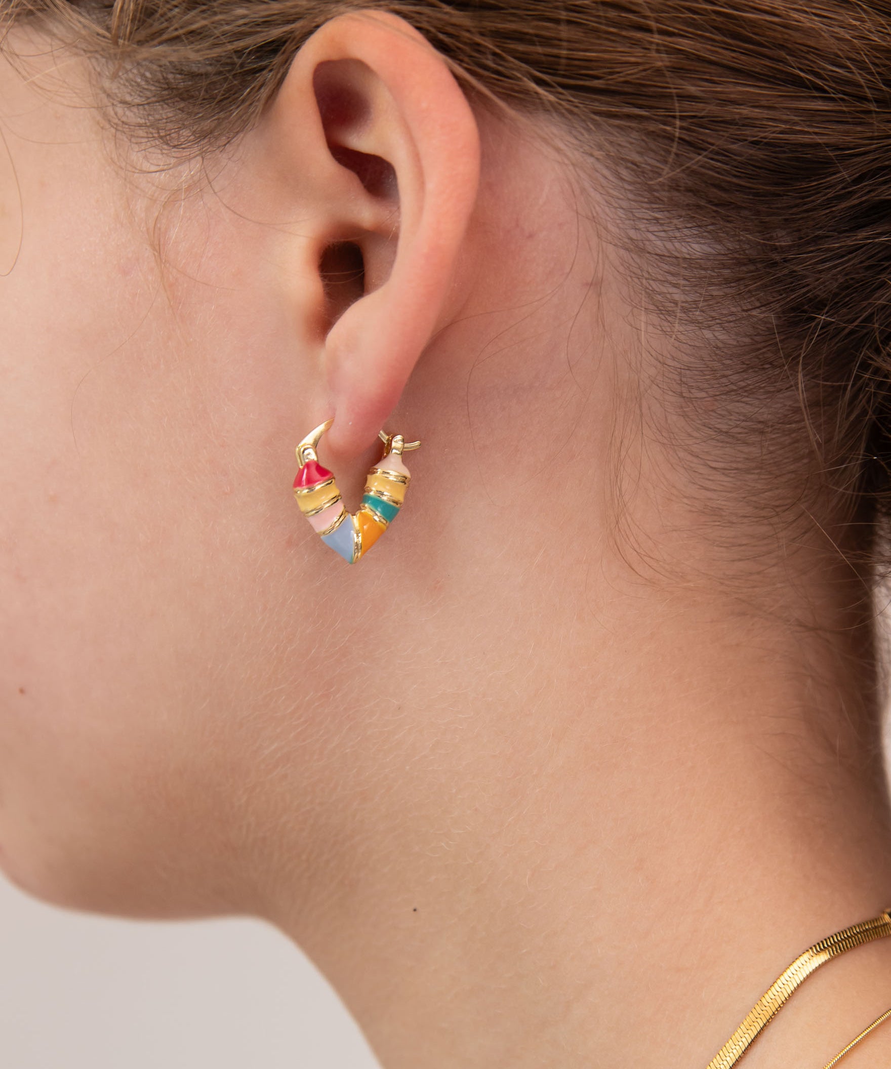 Close-up of a girl wearing colorful heart-shaped huggie earring by Kaleidoscope Living.
