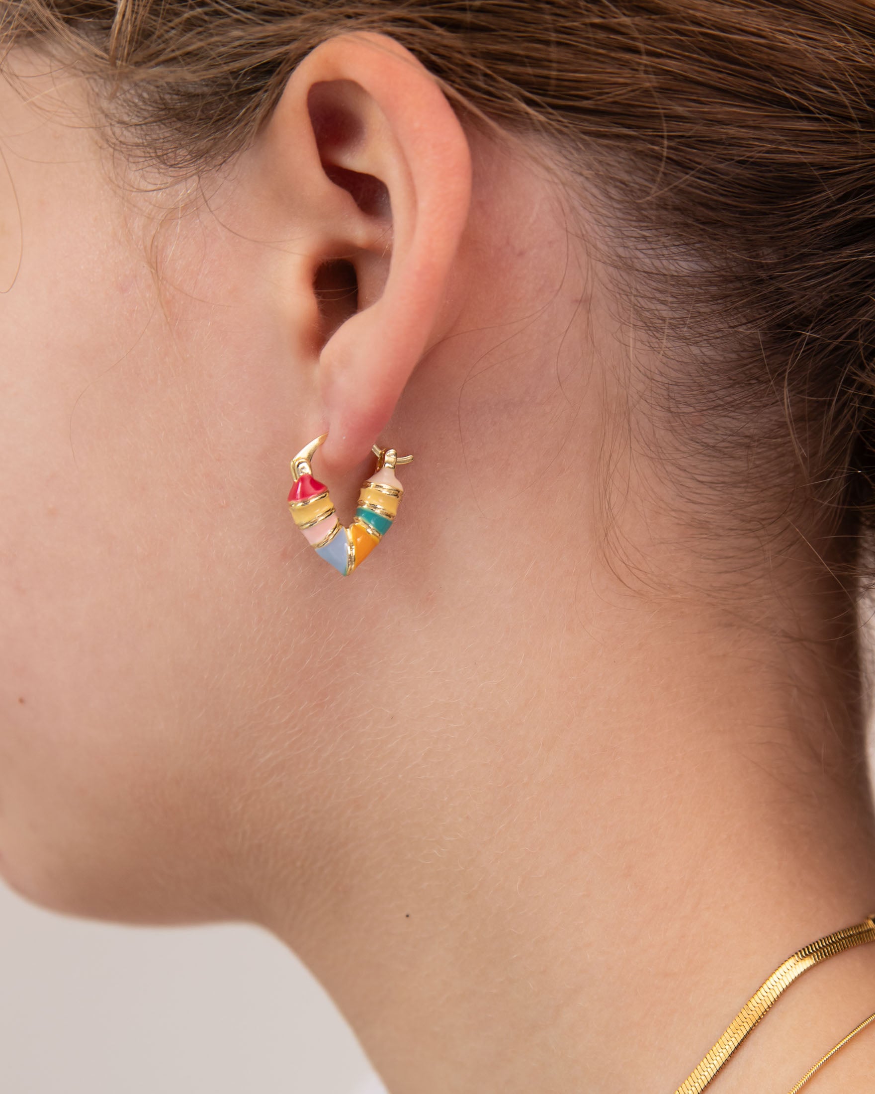 Close-up of a girl wearing colorful heart-shaped huggie earring by Kaleidoscope Living.