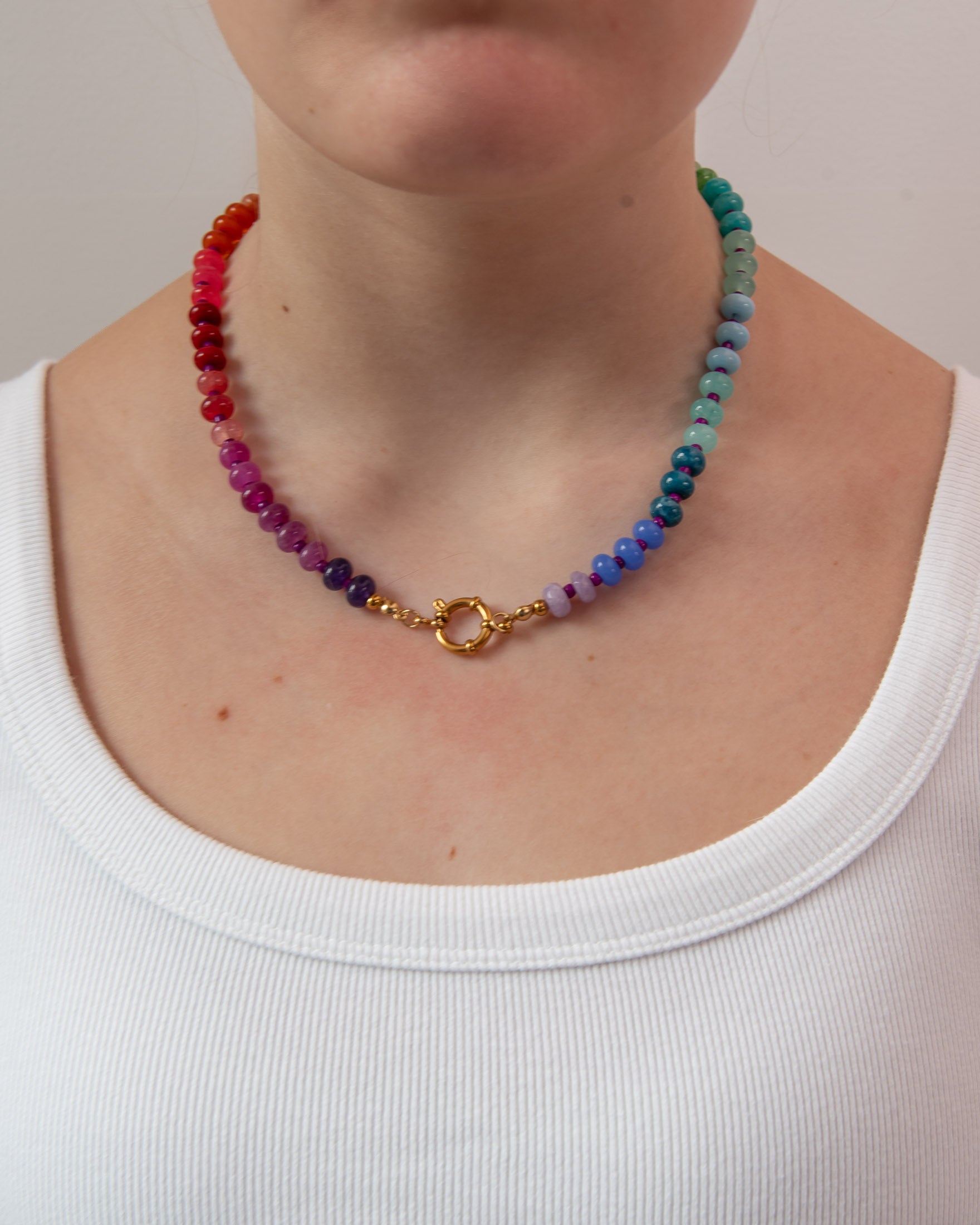Multicolored round beaded necklace with a gold clasp worn in front 