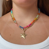 A close-up of a woman wearing a multi-strand necklace featuring colorful beads, a gold-tone paperclip chain, and a dangling star charm.