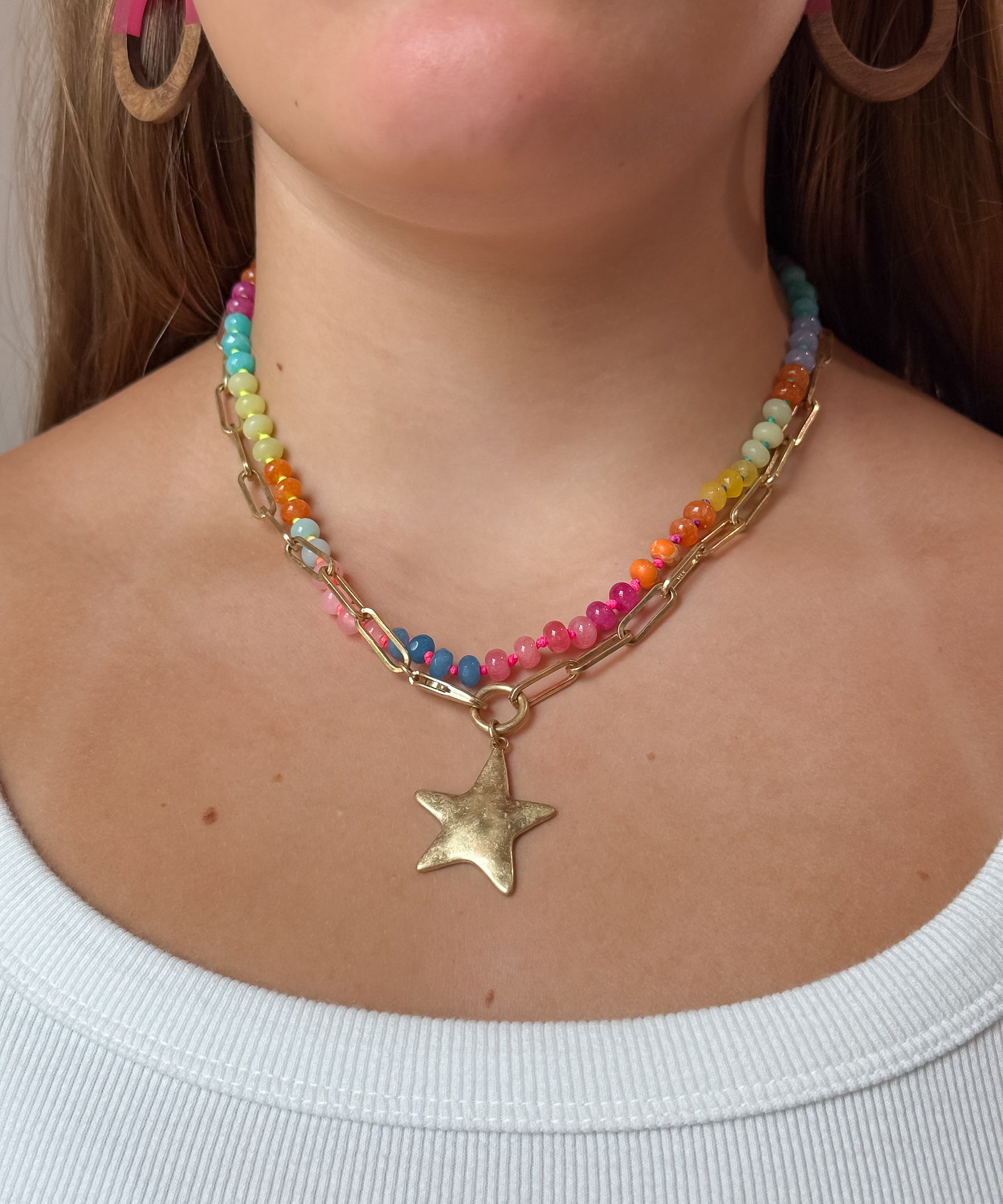 A close-up of a woman wearing a multi-strand necklace featuring colorful beads, a gold-tone paperclip chain, and a dangling star charm.