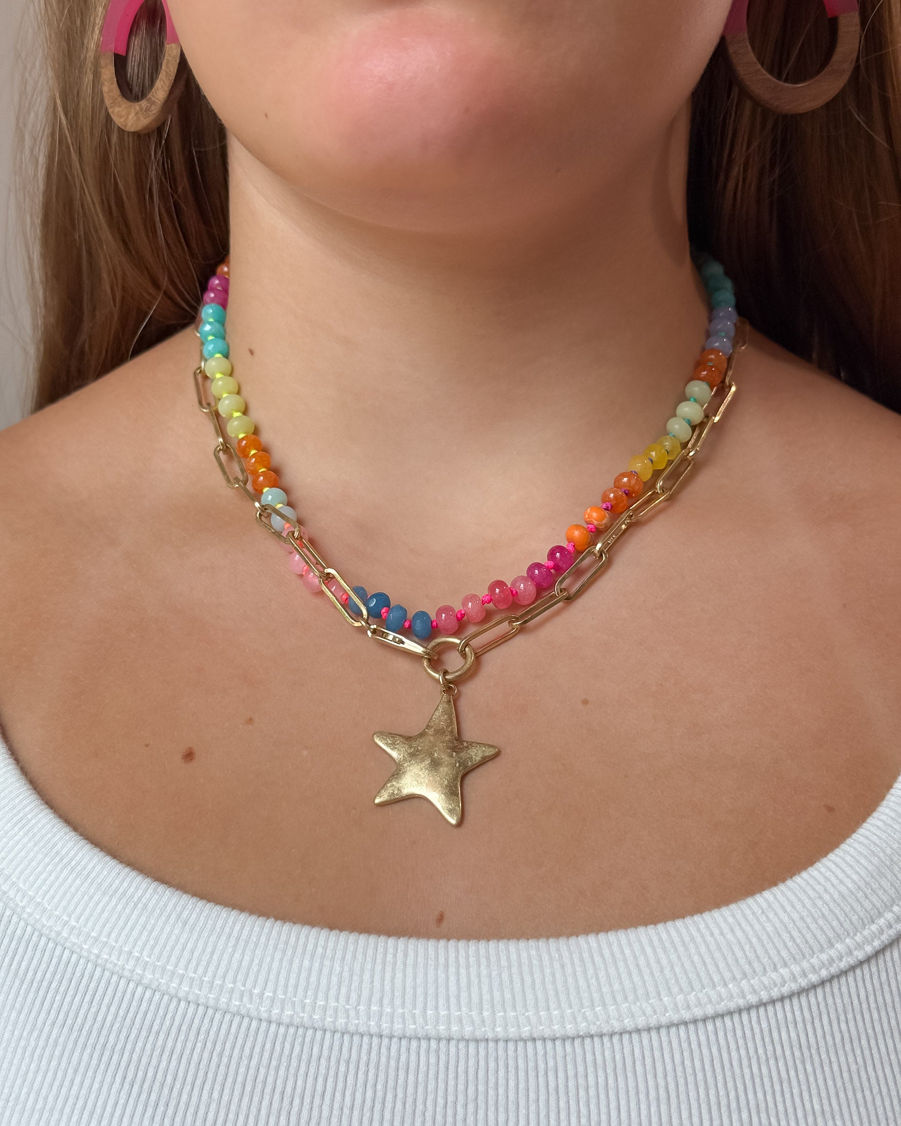A close-up of a woman wearing a multi-strand necklace featuring colorful beads, a gold-tone paperclip chain, and a dangling star charm.