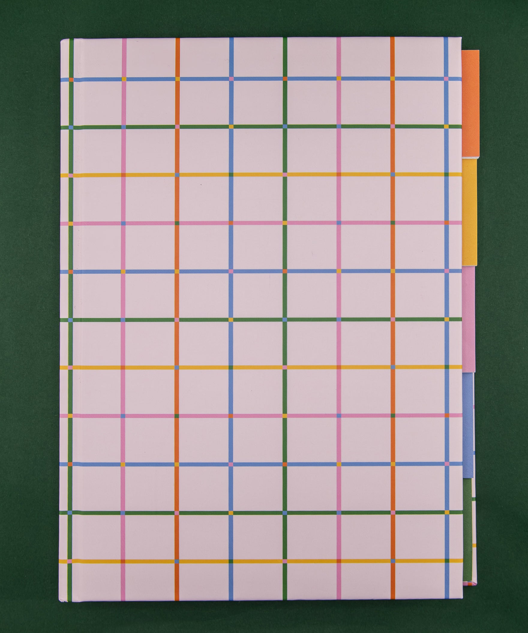 A hardcover notebook with a pale pink cover featuring a colorful plaid pattern and five colorful tabbed sections against a dark green background.