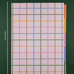 A hardcover tabbed notebook with a colorful plaid design of multicolored grid lines on a dark green background, showing dimension markers of 6.5 inches by 8.5 inches