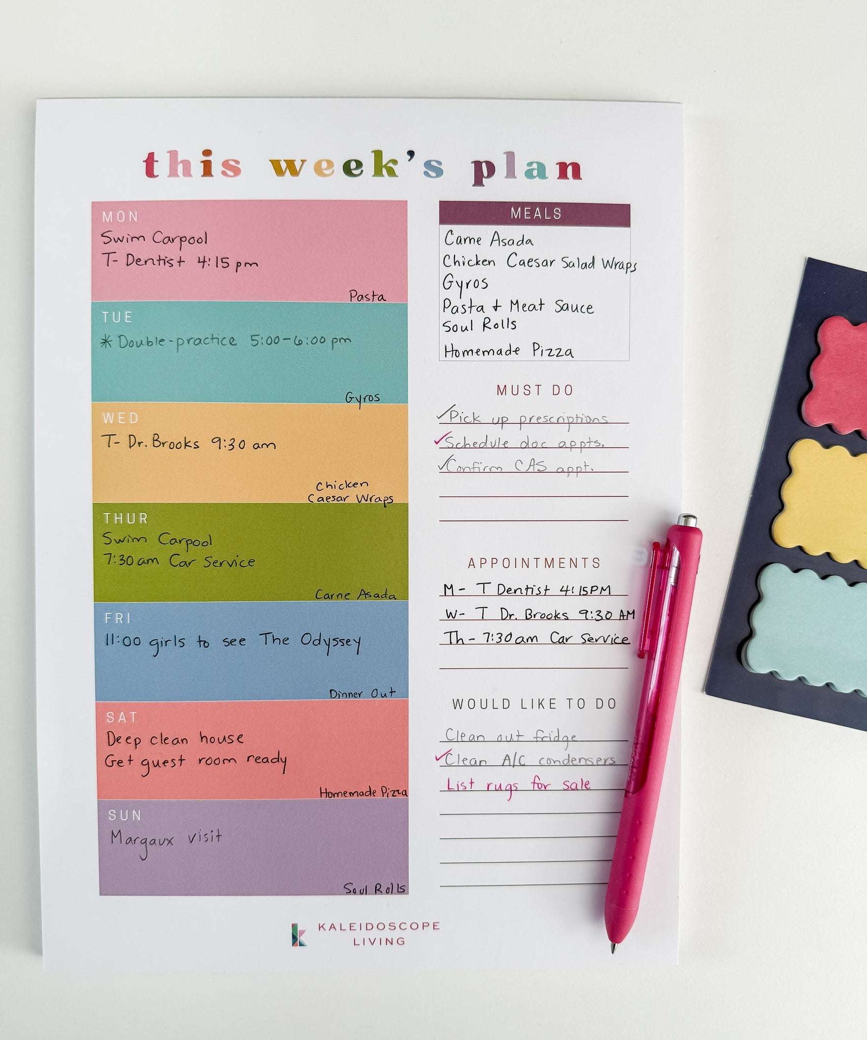 A weekly planner page from Kaleidoscope Living filled in with meals, appointments, and to-do lists, styled on a white background with a pink pen and colorful scalloped sticky notes on the side.