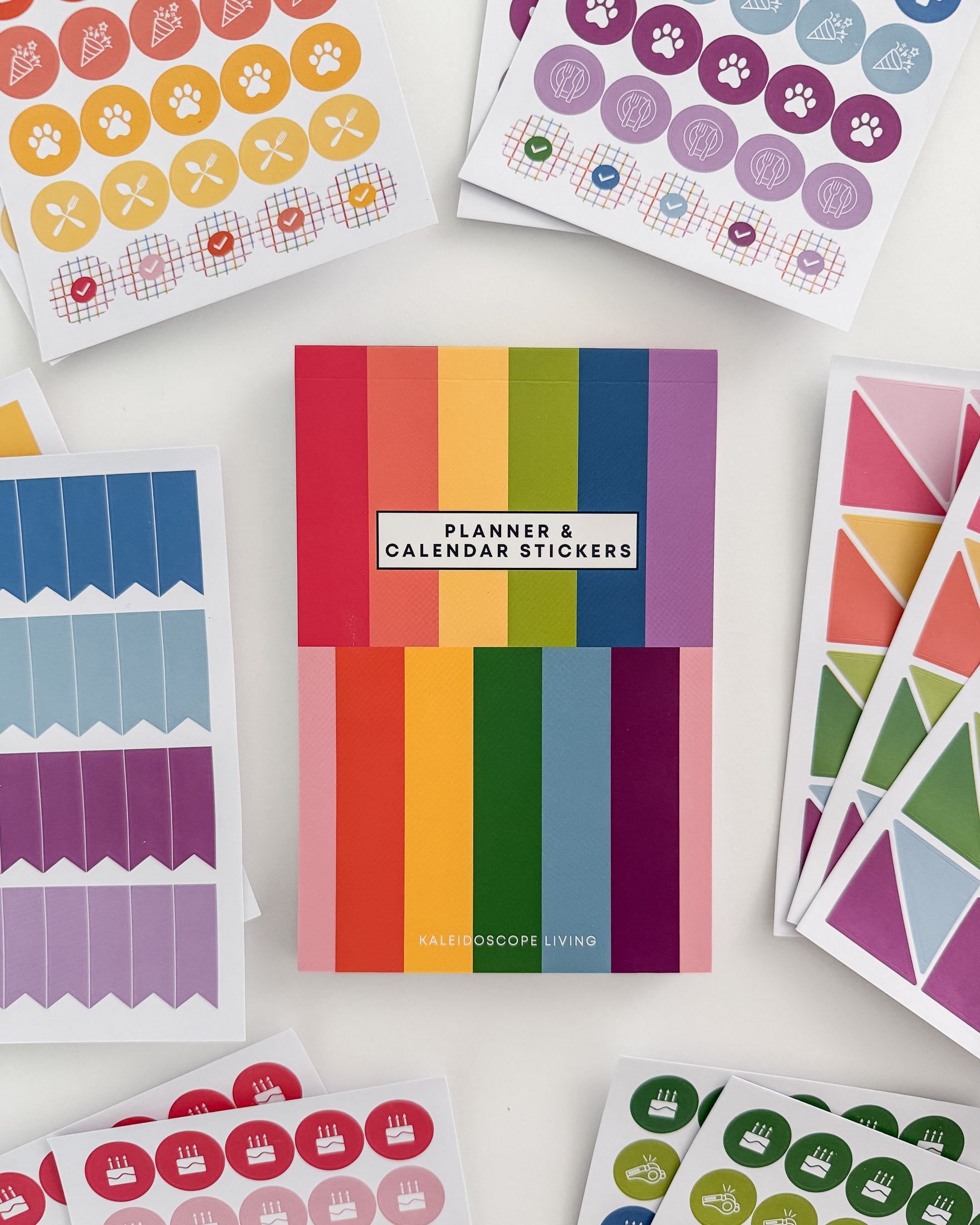 Close up view of Planner and Calendar Stickers top-bound sticker book surrounded by sticker pages featuring a variety of sticker designs in rainbow hues on white surface