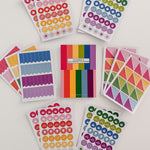 Full view of Planner and Calendar Stickers top-bound sticker book surrounded by sticker pages featuring a variety of sticker designs in rainbow hues on white surface