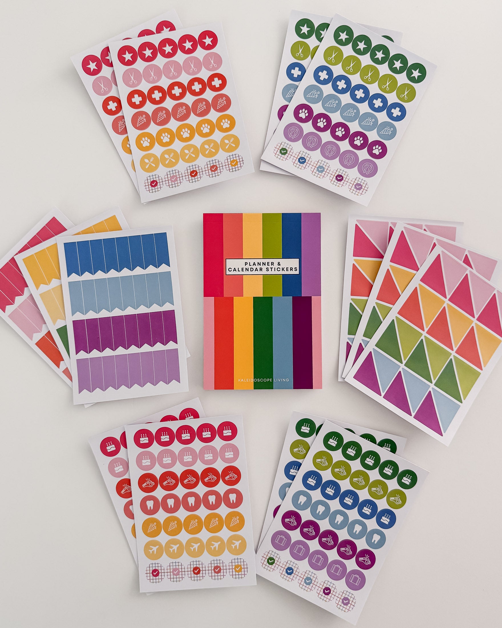 Full view of Planner and Calendar Stickers top-bound sticker book surrounded by sticker pages featuring a variety of sticker designs in rainbow hues on white surface