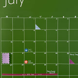 Photo of dark green July wall calendar with colorful planner and calendar stickers, scalloped sticky notes, and washi tape used to mark important appointments and events
