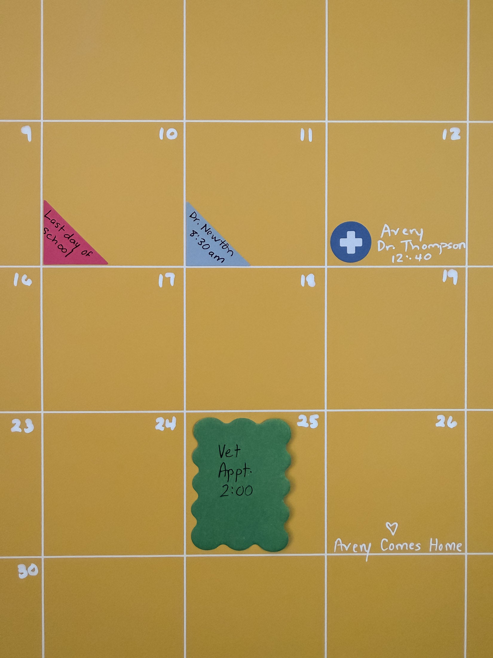 Close up view of yellow wall calendar with colorful planner and calendar stickers and scalloped sticky notes used to mark important appointments and events