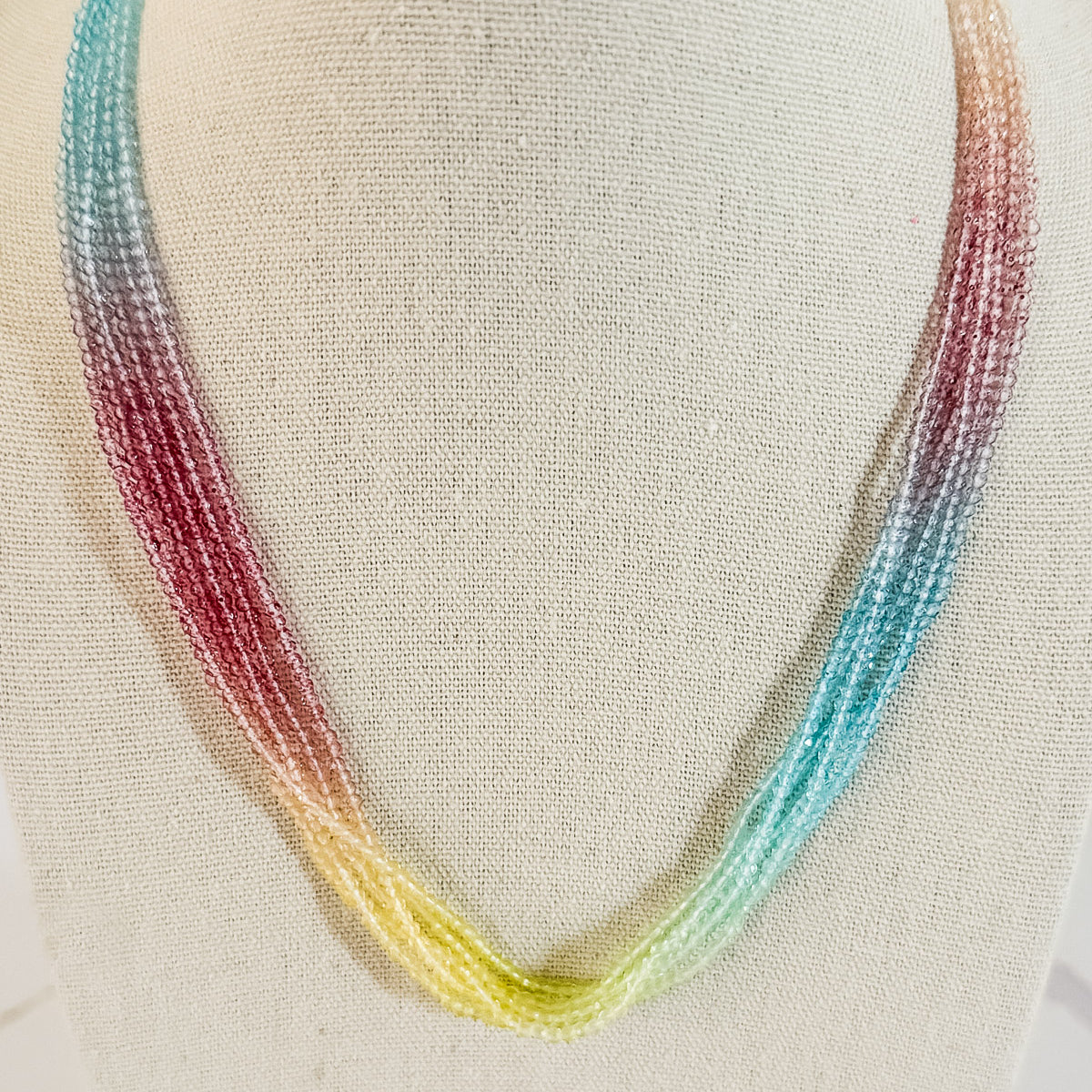 A layered glass seed bead necklace displayed on a mannequin, featuring beads in shades of pink, yellow, and blue.