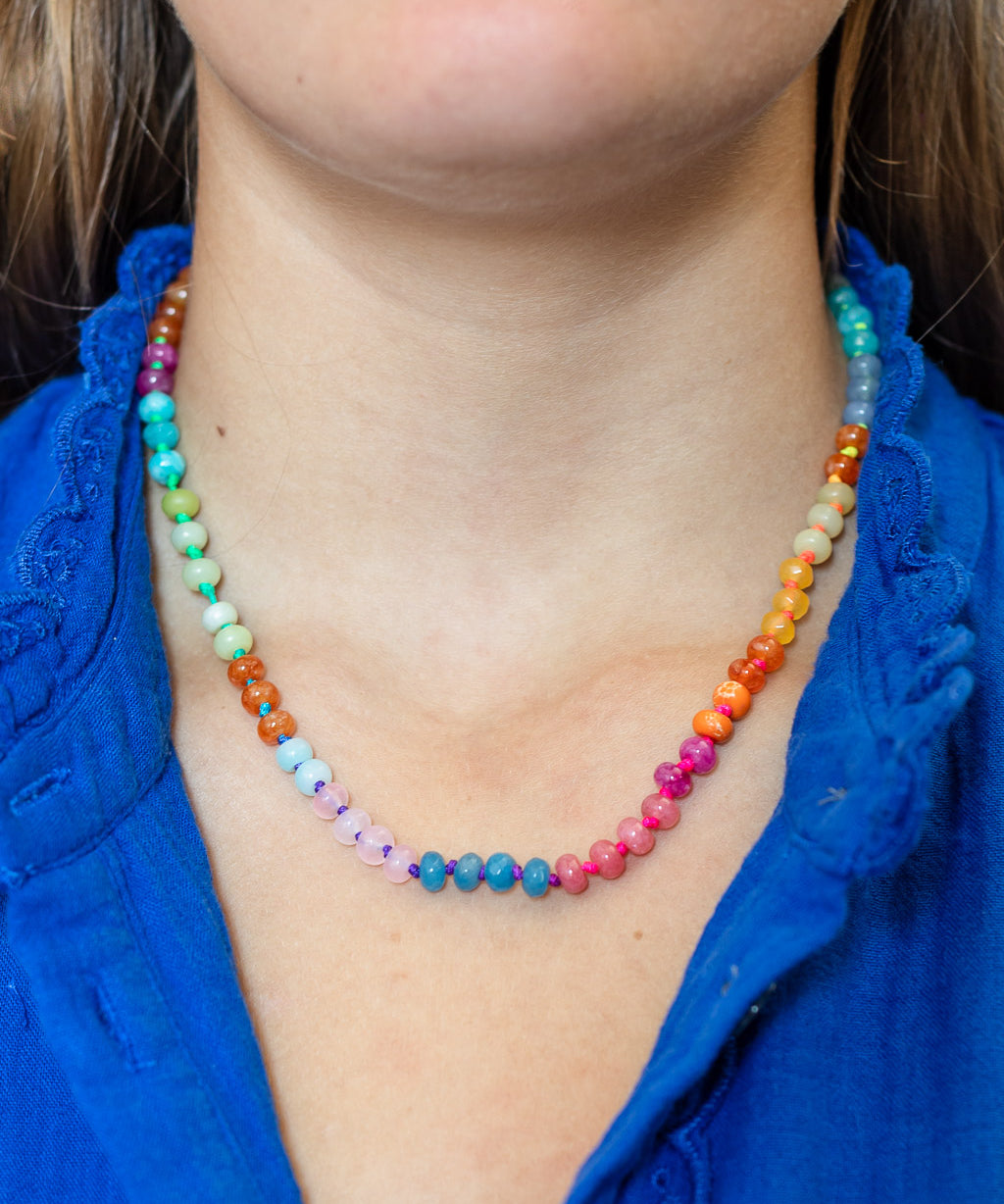 Close up of a colorful beaded necklace with neon color changing cord worn by a women with a blue shirt.