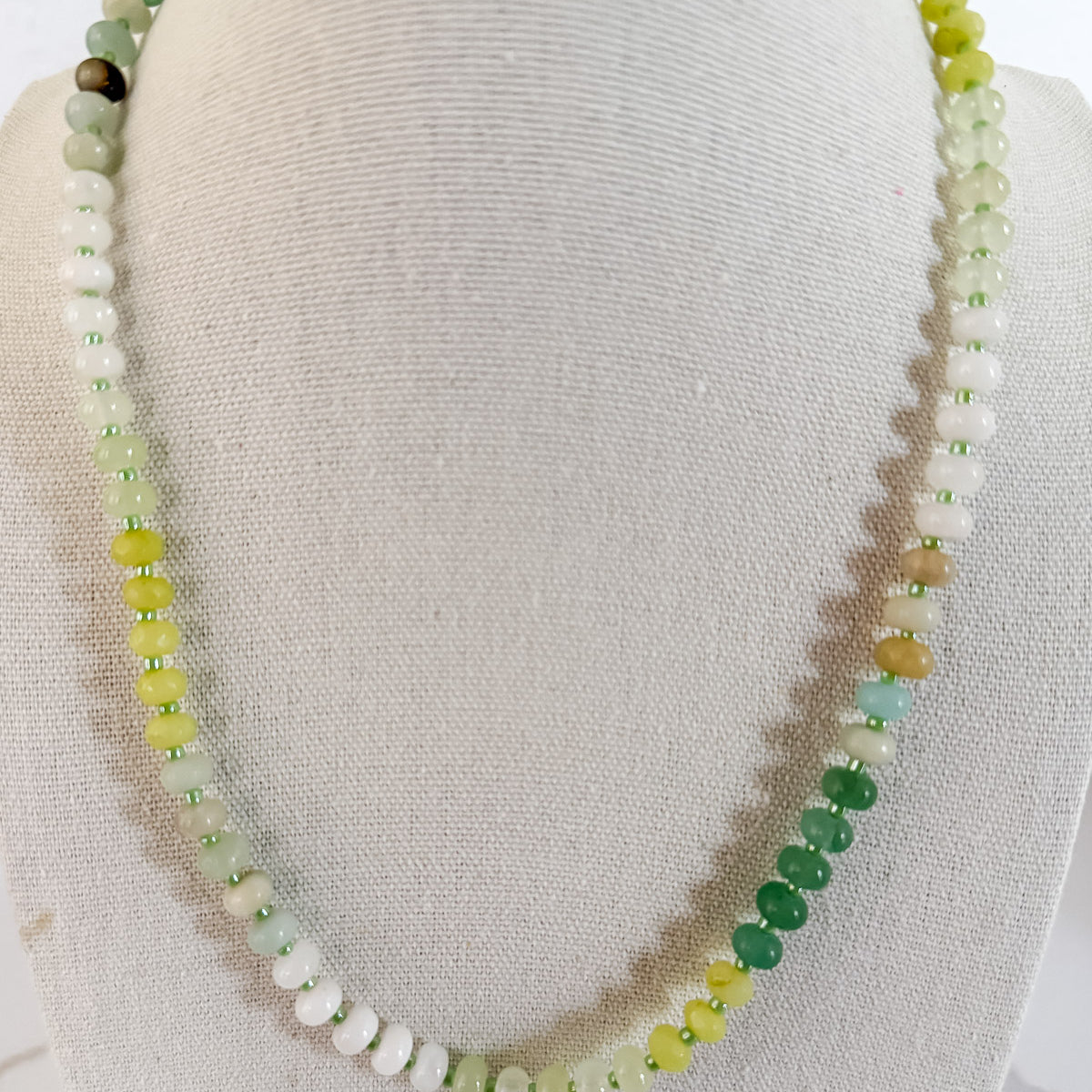 A beaded necklace with a gradient of natural stone beads in shades of green, displayed on a mannequin.