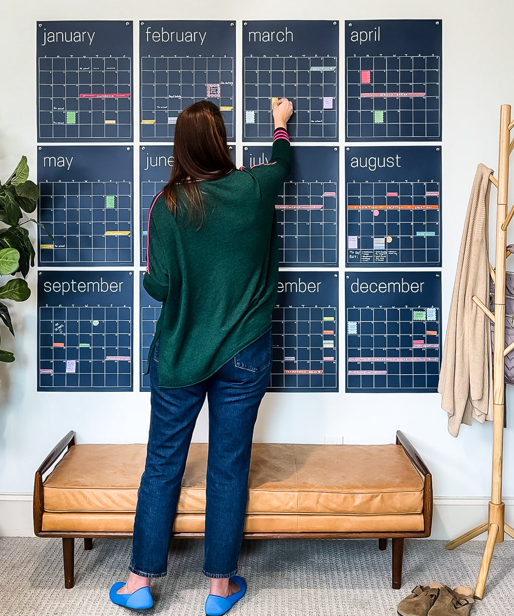 woman adding details to large reusable wall calendar in navy blue from Kaleidoscope Living