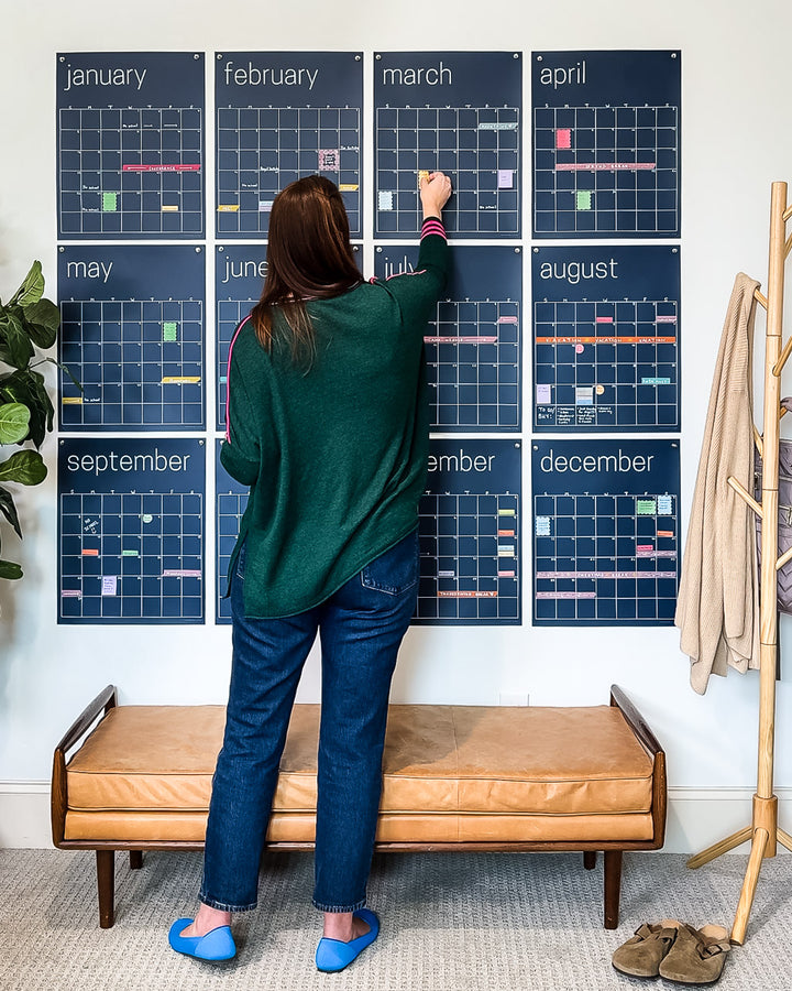 woman adding details to large reusable wall calendar in navy blue from Kaleidoscope Living