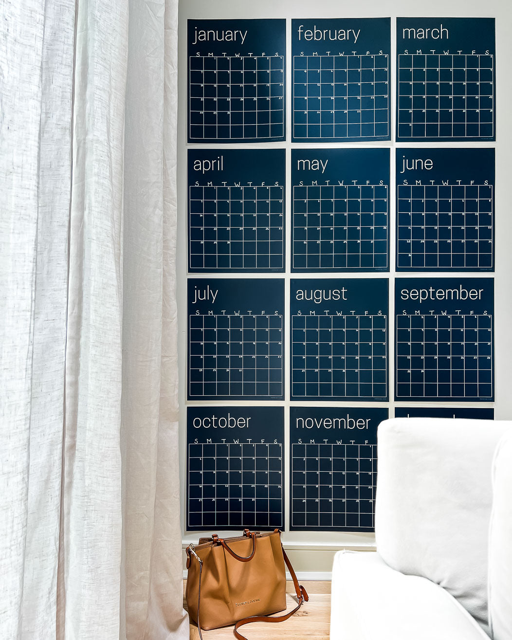 A series of large, navy blue, reusable wall calendar pages arranged in a grid format on a wall, with a tan big sitting on the floor in front of it.