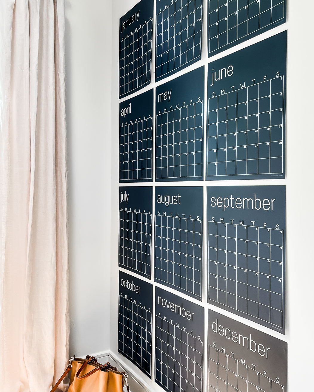 Twelve, large, navy blue, reusable wall calendar pages arranged in a grid format on a white wall.