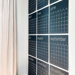 Twelve, large, navy blue, reusable wall calendar pages arranged in a grid format on a white wall.