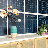Close up of the navy reusable wall calendar from Kaleidoscope Living displayed above a piece of furniture.