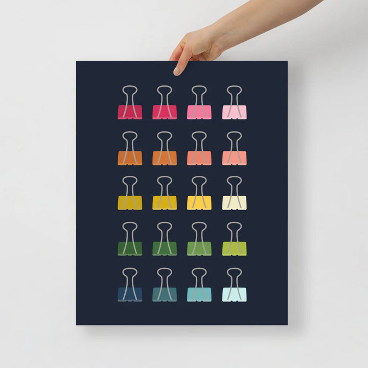 office art print with a navy background and grid of colorful clip art of binder clips in ombre rainbow colors ranging from pinks to blues