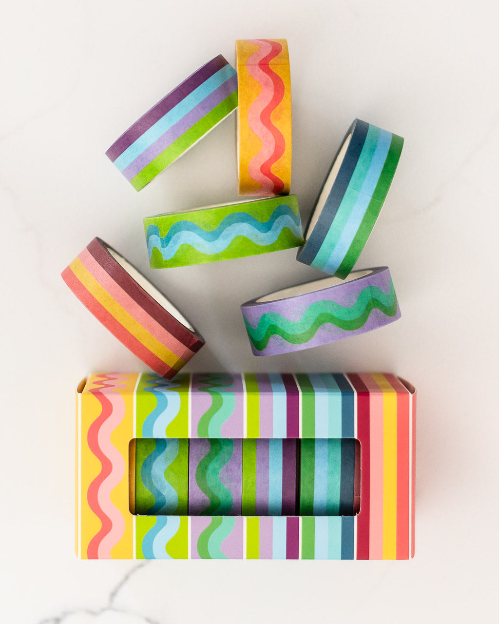 image of colorful striped and squiggle washi tape laying on white marble surface beside product box