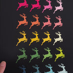 Video showing colorful Christmas and Winter themed art prints featuring graphics of familiar objects and symbols, like flying reindeer, a nativity scene, Christmas trees, angels and nutcrackers, arranged by color in symmetrical rows as follows: pink, orange, yellow, green and blue.
