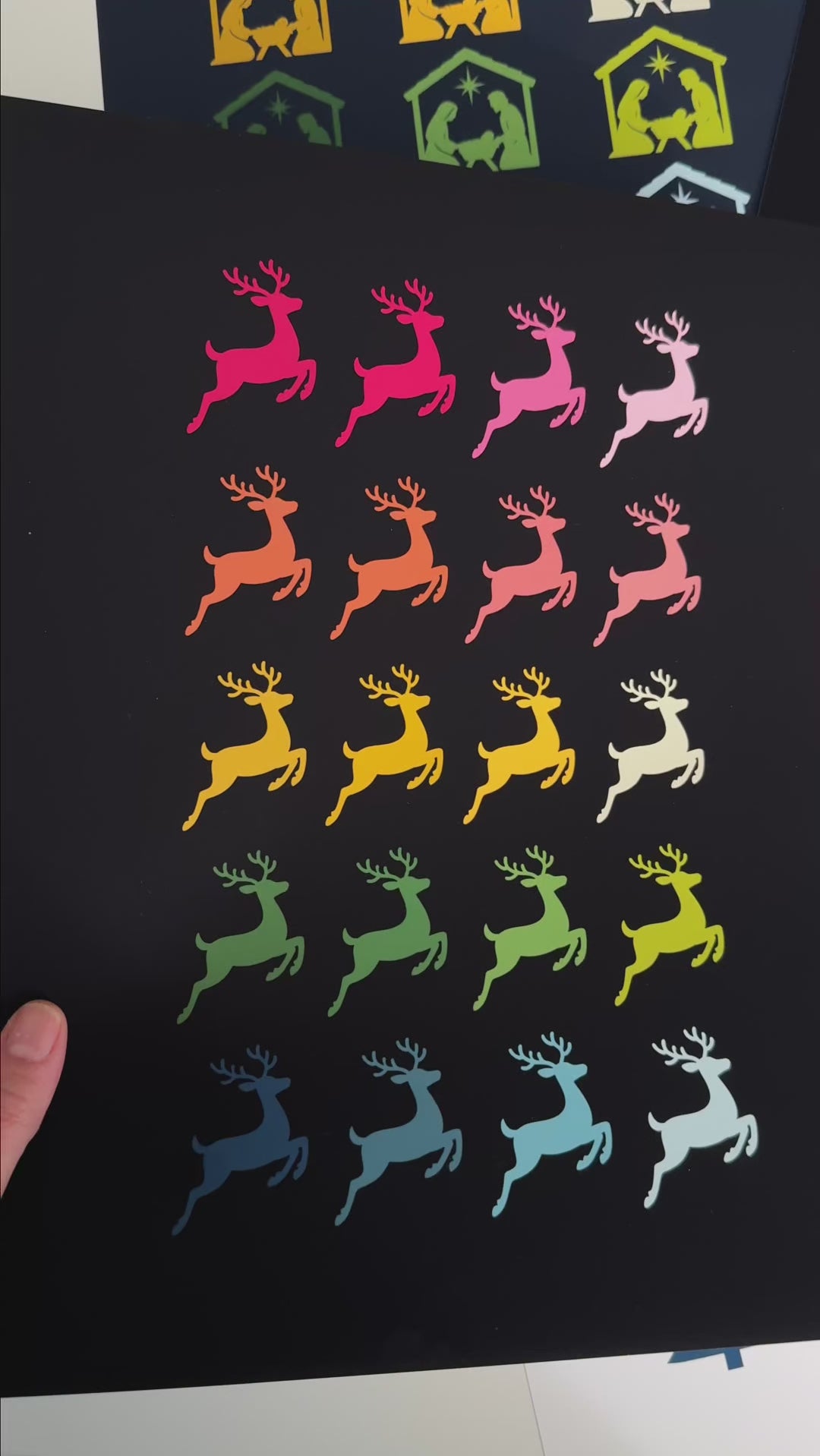 Video showing colorful Christmas and Winter themed art prints featuring graphics of familiar objects and symbols, like flying reindeer, a nativity scene, Christmas trees, angels and nutcrackers, arranged by color in symmetrical rows as follows: pink, orange, yellow, green and blue.