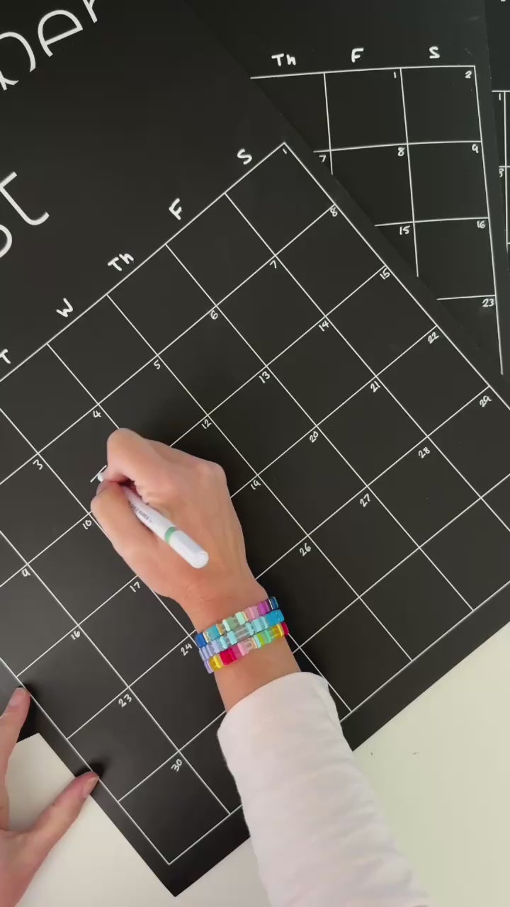 August page of a large black wall calendar showing the erasability of a white chalk marker