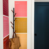 photo of 6 months of the large erasable wall calendar in colorful rainbow hues from Kaleidoscope Living hanging in corner of home near the door and a coat rack