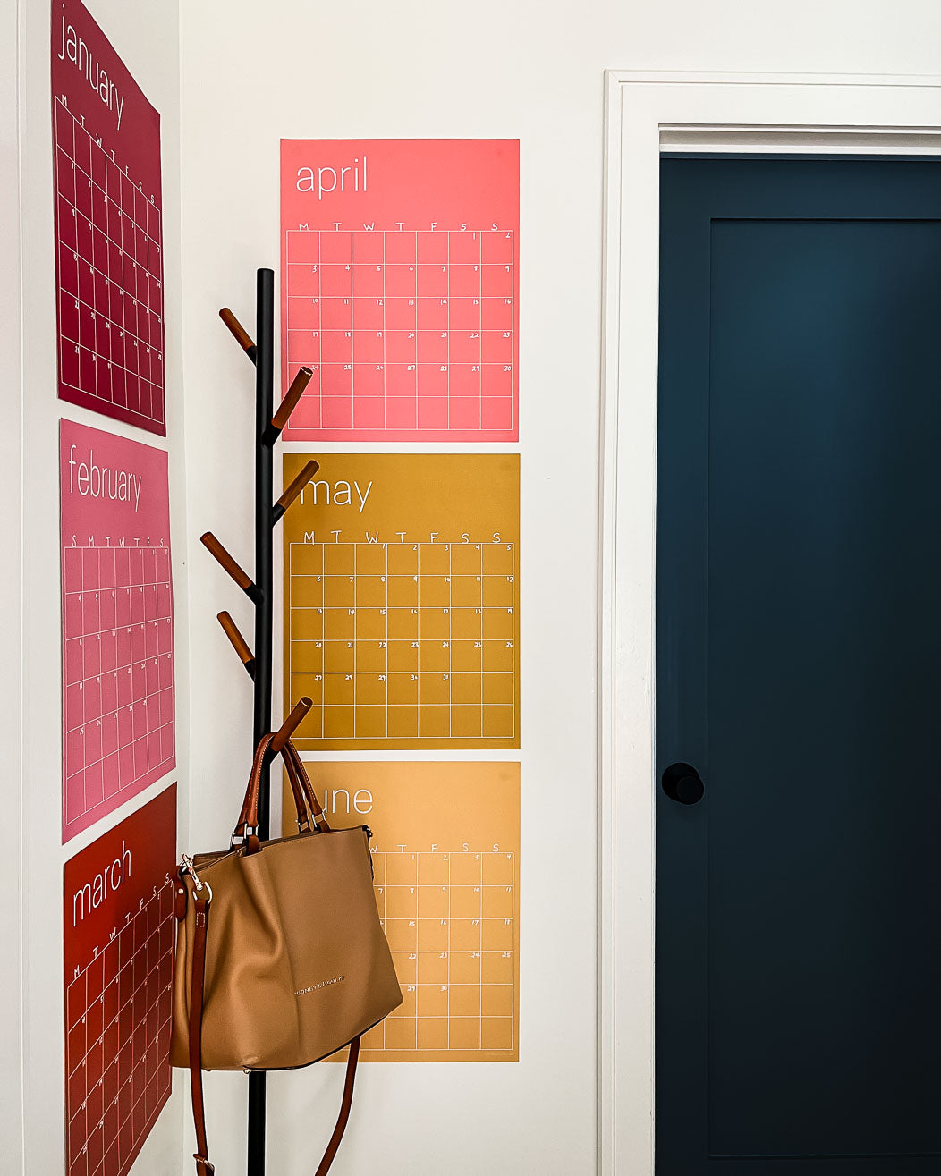 photo of 6 months of the large erasable wall calendar in colorful rainbow hues from Kaleidoscope Living hanging in corner of home near the door and a coat rack