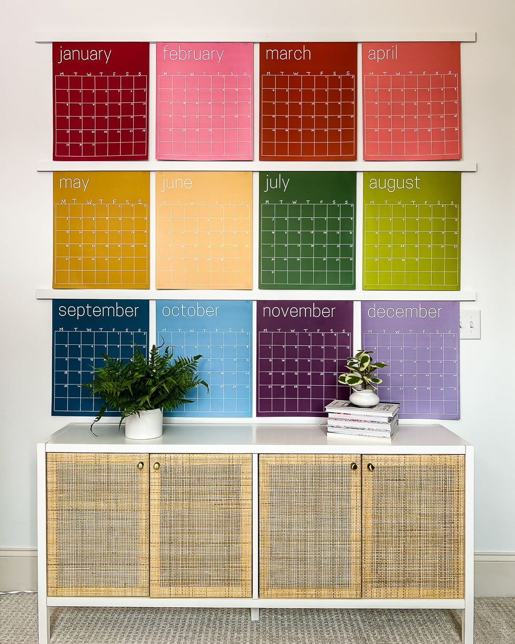 Large undated and reusable wall calendar in colorful rainbow hues from Kaleidoscope Living is hung over a dresser.
