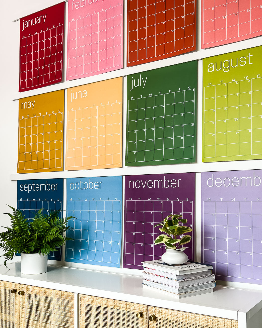Close up of the large undated and reusable wall calendar in colorful rainbow hues from Kaleidoscope Living hung with custom wood poster hangers.