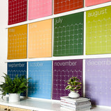 Close up of the large undated and reusable wall calendar in colorful rainbow hues from Kaleidoscope Living hung with custom wood poster hangers.