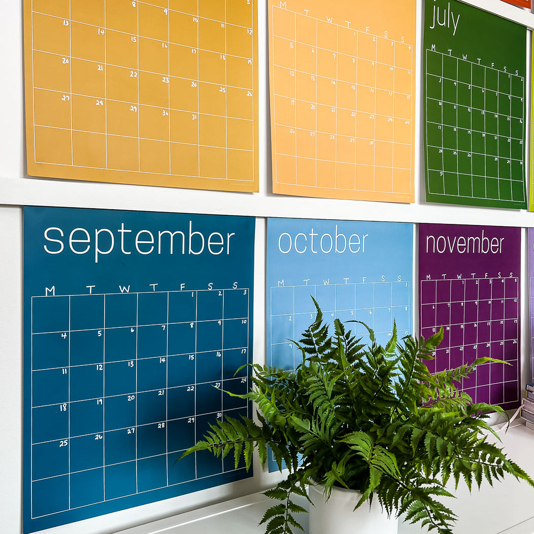 side view photo of large reusable wall calendar in rainbow colors from Kaleidoscope Living hanging above a console table
