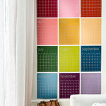 photo of large reusable wall calendar in colorful rainbow hues from Kaleidoscope Living hanging behind a sofa in a family room