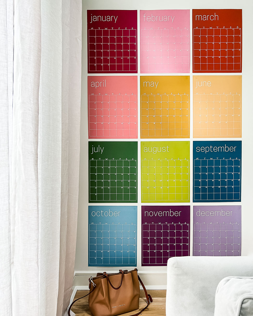 Reusable rainbow wall calendar with twelve individual pages hung on a white wall.