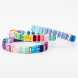 Stack of three colorful resin tile bracelets in blue, purple and rainbow hues with gold accents.