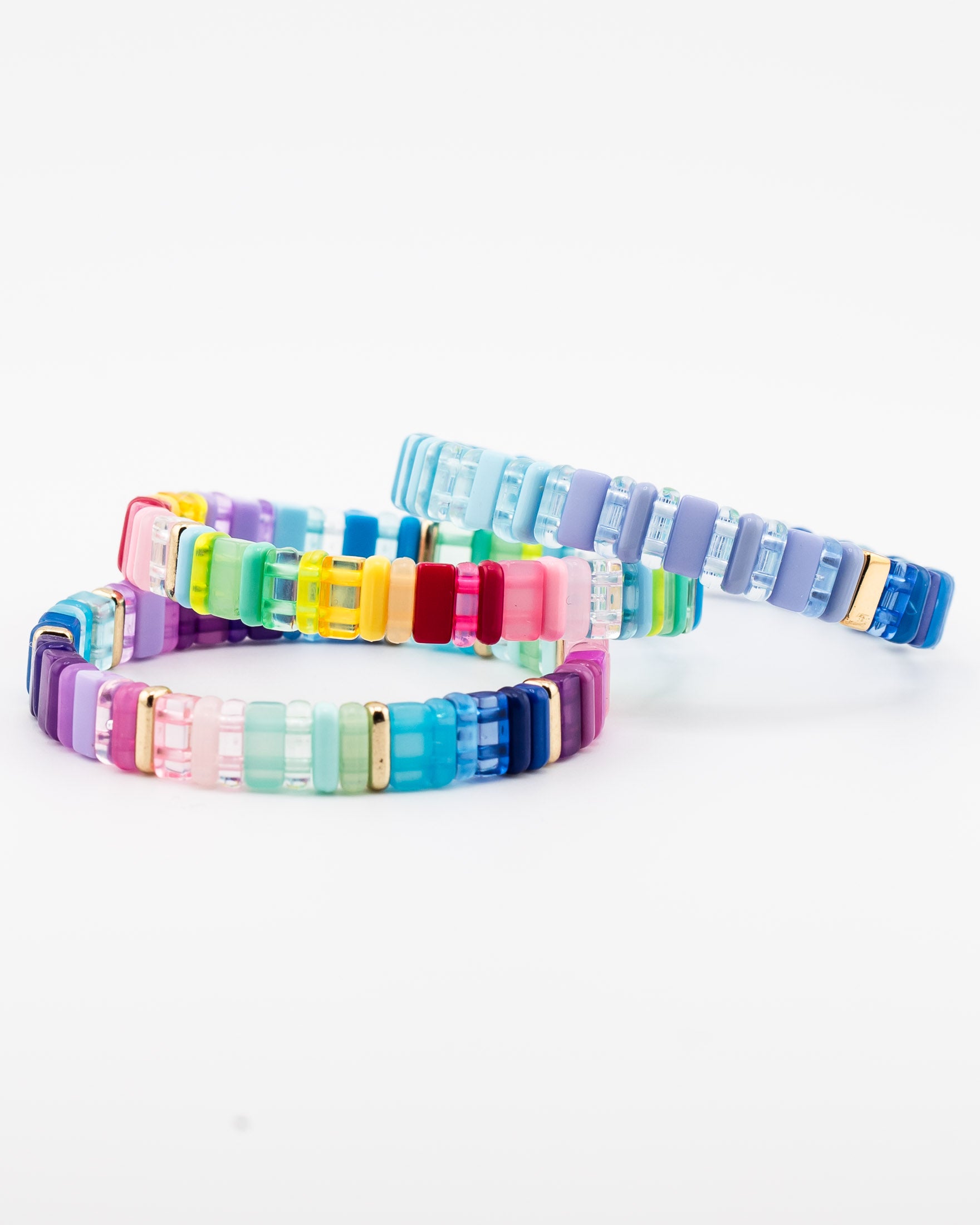 Stack of three colorful resin tile bracelets in blue, purple and rainbow hues with gold accents.